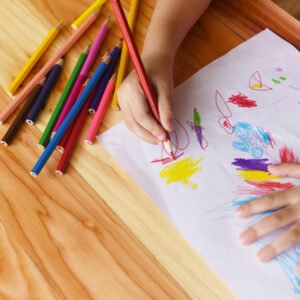 Girl painting on paper sheet with colour pencils on the wooden table at home / child kid doing drawing picture and colorful crayon