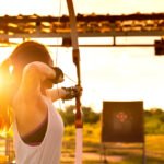 young female archer, archery, shoot arow with bow in nature field to target, success concept, at field for sport exercise at sunset time
