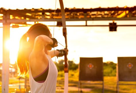 young female archer, archery, shoot arow with bow in nature field to target, success concept, at field for sport exercise at sunset time